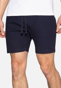 Mørkeblå badebukser lavet af blød stof, med snoreliv, lige pasform og subtil logo detalje ved kanten.