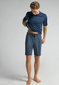 Dunkelblaues T-Shirt mit weicher Textur kombiniert mit gemusterten blau-grünen gestreiften Shorts, die einen elastischen Bund und einen Kordelzug haben.