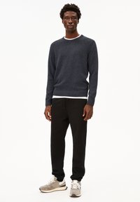 Un pull en tricot marine avec un col blanc, un pantalon de survêtement noir et des baskets grises. La tenue présente une coupe décontractée et un tissu texturé.