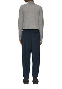 Un pull col roulé gris en tricot associé à un pantalon en velours côtelé bleu foncé, présentant une coupe décontractée et une poche latérale, complété par des bottes noires.