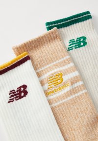 Tri par socks s rebrastom teksturom. Boje uključuju bijelu s maroon detaljima, narančastu s bijelim trakama i logotipom, te bijelu s zelenim trakama.