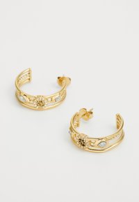 Boucles d'oreilles en ton or, avec des designs découpés complexes, ornées de cristaux transparents et de motifs floraux. Fermeture à tige sécurisée.