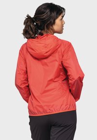 Rot, leicht, wasserdichte Jacke mit Kapuze, elastischen Bündchen und gerafftem Saum. Glatte Textur, minimalistisches Design, rückwärts getragen.