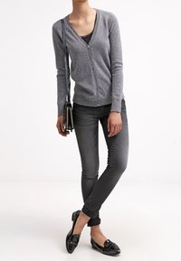 Grå stickad cardigan med v-ringning, knappstängning, i kombination med mörkgrå skinny jeans och svarta loafers. Svart axelremsväska i detalj synlig.