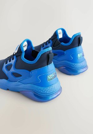 Modré sportovní boty s hladkým syntetickým svrškem, navržené v kombinaci modrých odstínů a průhledných gumových podrážek. Disponují logem na patě.