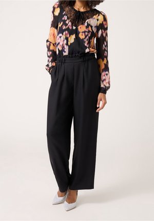 Bluzka w kwiatowy wzór z długimi rękawami i koronkowym kołnierzykiem, zestawiona z czarnymi spodniami o wysokim stanie. Na koniec stylizacji błyszczące czółenka w szpic.