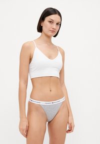 Valge sportlik bralet, millel on peened rihmad ja V-kaelus, koos hallide stringide alusriiete komplektiga, millel on valge bränditud vöökoht.