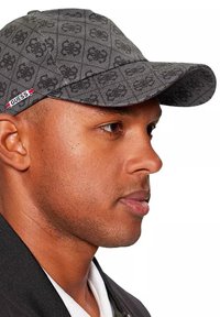 Cappellino nero con motivo e logo, che mostra la texture del tessuto e la visiera curva. Presenta un'etichetta rossa e bianca sul lato.
