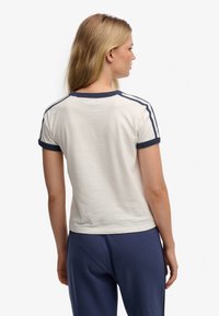 Wit katoenen T-shirt met marineblauwe biezen, korte mouwen en zijstrepen. De achterkant is glad met een ronde halslijn.