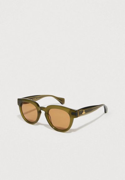 Lunettes de soleil vert olive avec des verres marron, de forme carrée arrondie, et un accent doré sur la branche. Monture transparente avec finition brillante.
