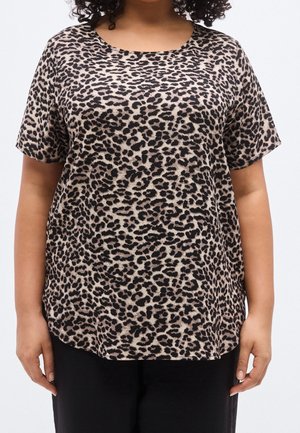 Vrouw draagt een beige-zwart kortemouwen luipaardprint blouse met een ronde halslijn en een zwarte broek tegen een effen achtergrond.