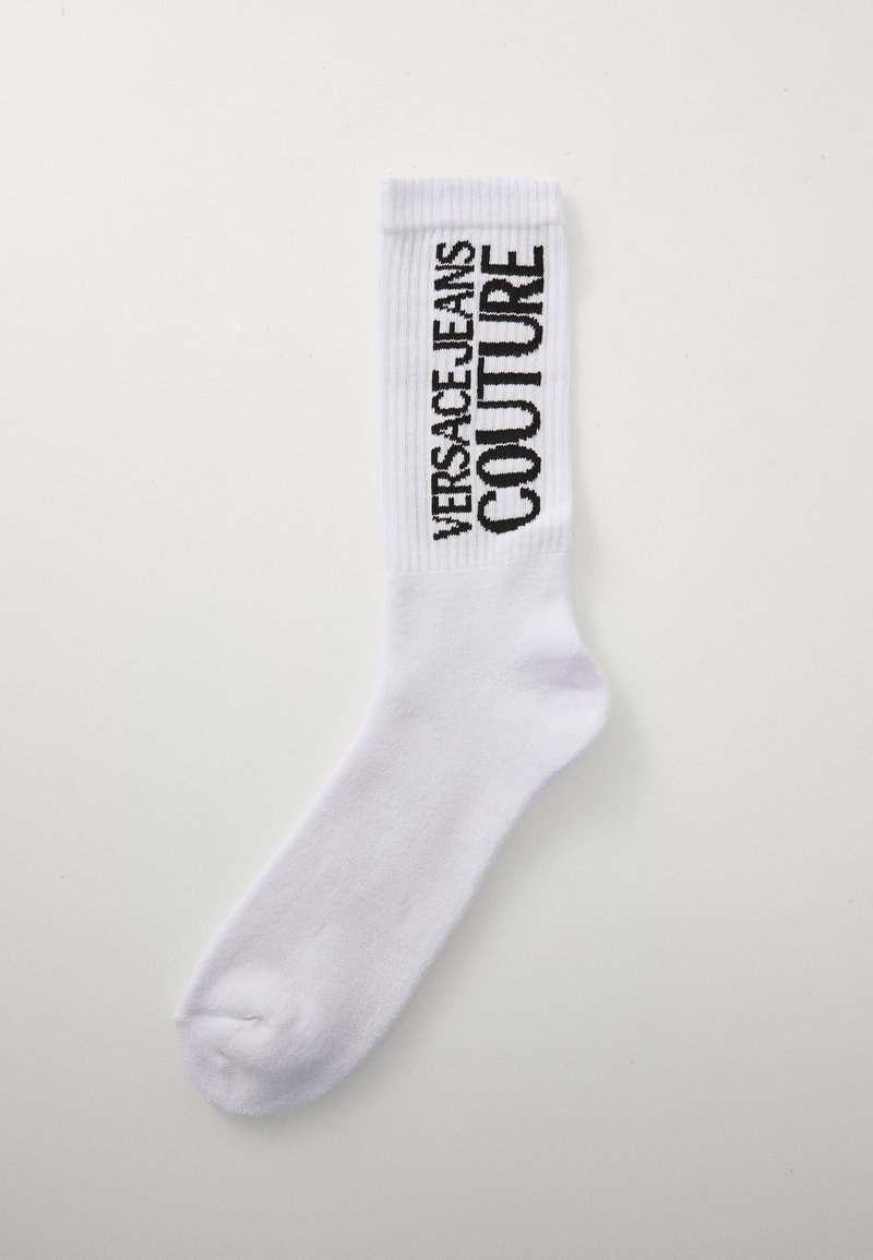 Calcetín blanco de crew con puño acanalado que presenta el logotipo vertical en negro de Versace Jeans Couture sobre un fondo liso.