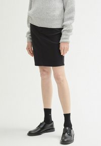 Schwarzer Bleistiftrock mit taillierter Passform, featuring einen Knopfverschluss vorne. Kombiniert mit einem grauen Strickpullover und schwarzen Lederschuhen.