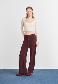 Dlouhé, burgundské pletené kalhoty s texturou a uvolněným střihem, se stahovací šňůrkou v pase, v kombinaci s úzkým, světlým topem s dlouhým rukávem.