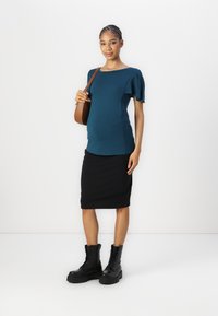 Tealfärgad kortärmad topp med utsvängda detaljer, kombinerad med en svart pennkjol och svarta snörda kängor. Modellen bär en brun handväska.