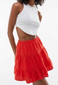 Top corto bianco in tessuto a coste, abbinato a una gonna rossa a strati con vita elastica e tessuto leggero.