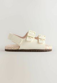 Sandales jaune clair en matière synthétique, avec deux boucles réglables, une semelle intérieure beige texturée et une semelle extérieure marron.