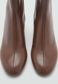 Botas de cuero marrón hasta el tobillo con un acabado suave, forma estilizada, costuras verticales y punteras redondeadas, presentadas desde una vista superior.