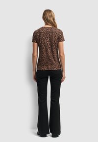 Koszulka w panterkę w kolorze brązowym i czarnym, z krótkimi rękawami i okrągłym dekoltem, zestawiona z czarnymi spodniami w stylu dzwonów i czarnymi butami.