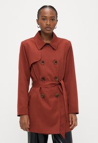 Rdeč dvoredni trench plašč z zavezovanjem v pasu, velikim ovratnikom in rjavimi gumbi. Iz gladkega materiala s strukturiranim dizajnom.