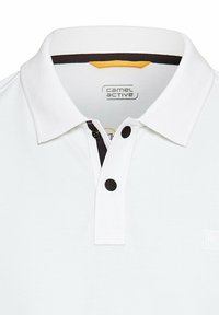 Hvid polo shirt med tekstureret stof, med en placket med tre knapper og en kontrasterende mørk kraveaccent. Camel Active logoet vist.