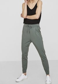 Ljusgröna joggers med elastisk midja och dragsko. Tillverkade av mjukt tyg med sidofickor och smalnande anklar. Bärs med en svart linne.