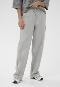 Helehallid dressipüksid lõdva lõikega, nöörkinnitusega vöökohaga ja vertikaalsete õmblusega, sobitatud heledate spordijalatsitega.