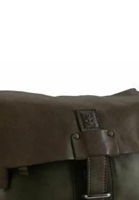 Borsa a tracolla in pelle marrone con chiusura a patta, caratterizzata da un logo a forma di ancora in metallo, borchie e dettagli di cucitura sulla parte anteriore.