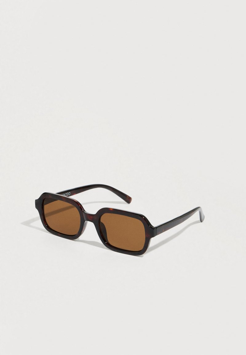 Lunettes de soleil teintées marron avec une monture épaisse octogonale en écaille de tortue marron et des branches noires élégantes. Design minimaliste sans logos visibles.
