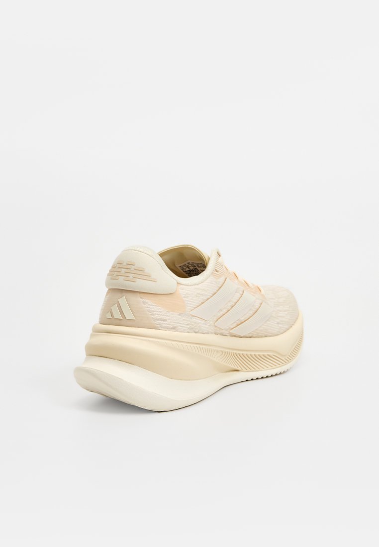 Zapatilla deportiva beige con parte superior de malla texturizada, diseño de tres rayas en blanco, suela acolchada y un discreto detalle de logo en el talón.