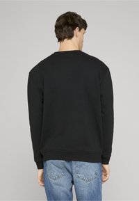 Crna majica s okruglim izrezom i spuštenim ramenima, s glatkom teksturom. Upotpunjena svijetloplavim trapericama.