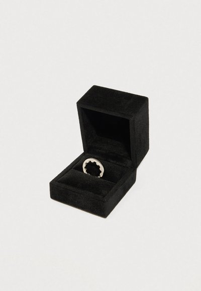 Stříbrný prsten se zvlněným okrajem, vystavený v černé sametové šperkovnici s měkkým vnitřkem pro ochranu.