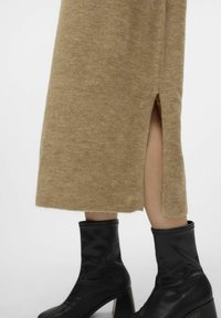 Robe en tricot beige avec ourlet côtelé et fente latérale, associée à des bottines noires à talon épais. Texture lisse, design moderne.