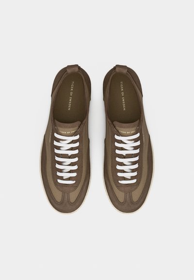 Pari ruskeita rentoja tennareita valkoisilla nauhoilla, merkitty "Tiger of Sweden", nähtynä ylhäältä vaaleanharmaalla taustalla.