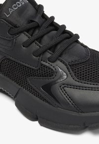 Zapato deportivo negro con parte superior de malla y cuero sintético, punta redondeada, acentos texturizados y cordones planos, que cuenta con una suela acolchada.