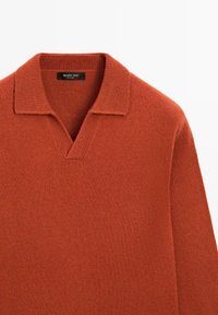Rdzawy sweter dzianinowy z dekoltem w serek i krótkim, płaskim kołnierzykiem. Tekstura jest miękka i gładka, wykonana z cienkiego, ciepłego materiału.