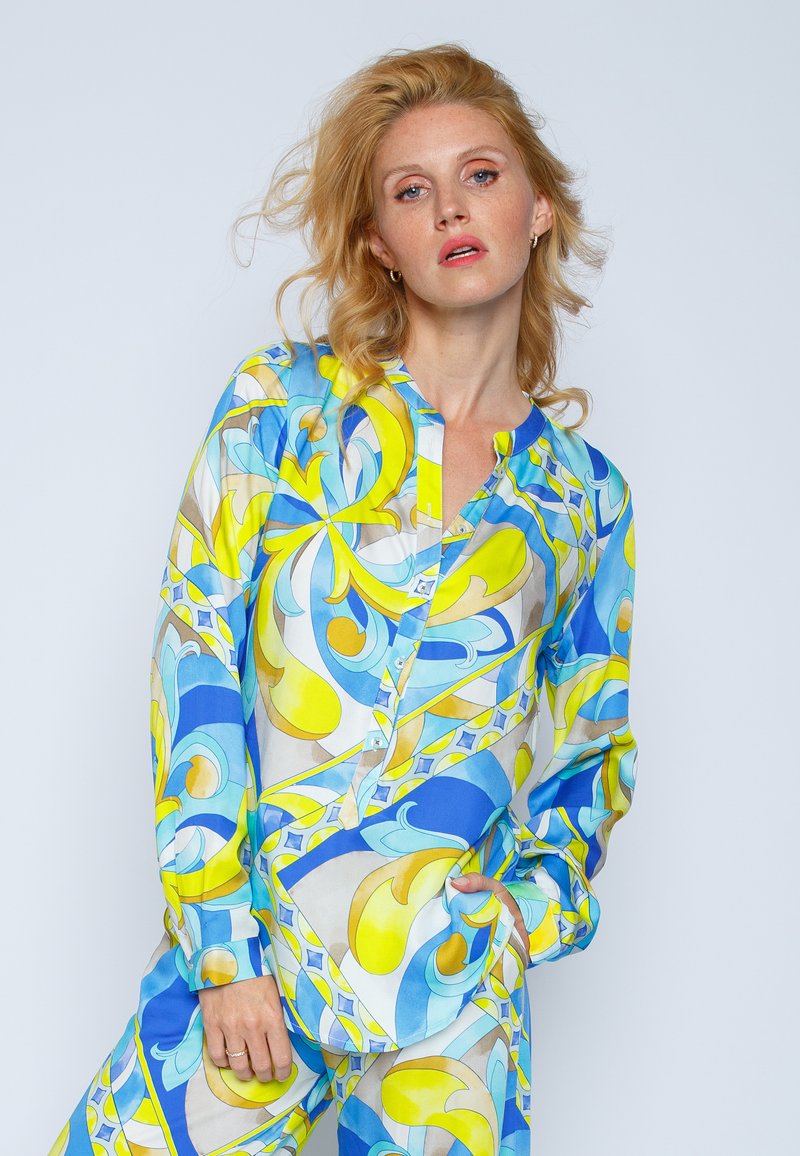 Koszula z długim rękawem, zapinana na guziki, w niebiesko-żółty abstrakcyjny wzór, wykonana z gładkiego materiału; ma okrągły dekolt i mankiety z zapięciem.
