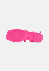 Semelle en caoutchouc rose avec texture antidérapante, présentant une surface lisse et une zone marquée. Les accents comprennent des sangles multicolores pour un détail supplémentaire.