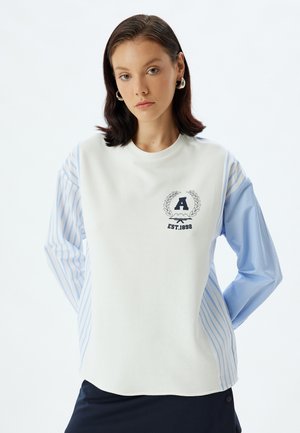 Witte sweatshirt met lichtblauwe gestreepte lange mouwen en een ronde halslijn. Bevat een embleem met de letter "A" en "EST. 1892" erop gedrukt.