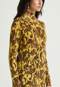 Maglione giallo a maniche lunghe con collo alto, caratterizzato da un motivo floreale in marrone scuro e rosa, realizzato in un tessuto a maglia testurizzato.