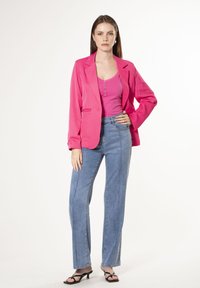 Blazer rosa brillante sobre una camiseta a juego, combinado con jeans de tiro alto en azul claro con costuras prominentes y sandalias de tacón negras.