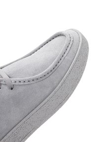Zapato de ante gris con punta redondeada y suave, costuras a tono y suela de goma texturizada con un patrón moteado.