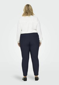 Balta garām piedurknēm krekls ar saplacinātiem aprocēm kombinācijā ar pieguļošām tumši zilām biksēm, kas aprīkotas ar divām aizmugurējām kabatām un gludu tekstūru. Melni apavi ar kniedēm.