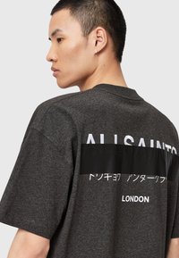 T-shirt en coton gris foncé avec un col rond, des manches courtes, et un texte et des graphiques blancs audacieux imprimés au dos.