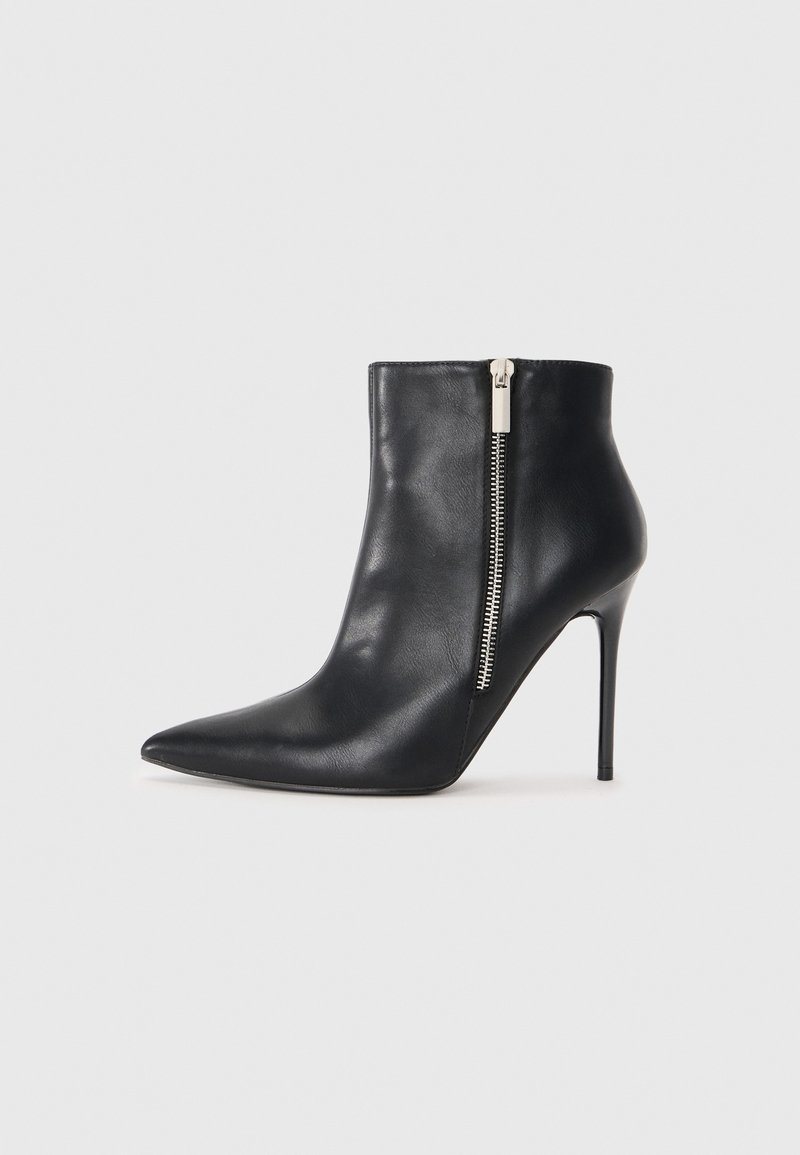 Bottine noire en cuir avec bout pointu, fermeture éclair latérale argentée et talon haut stilettos sur un fond clair uni.
