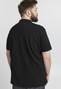 Černé polo tričko vyrobené z měkké látky, s klasickým límečkem a krátkými rukávy. Design je jednoduchý, bez viditelných vzorů nebo akcentů.