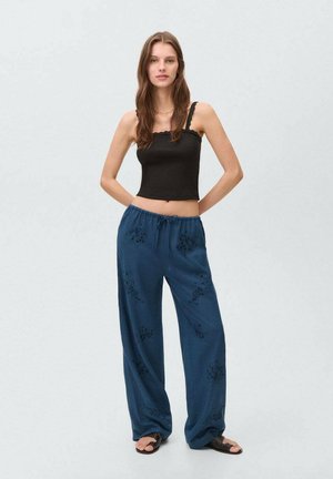 Zwarte crop top en losse donkerblauwe broek met bloemenborduursel. De broek heeft een elastische taille en een relaxte pasvorm.