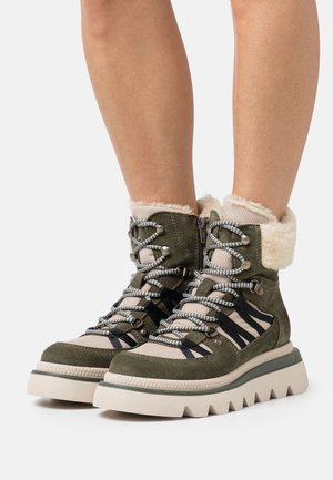 Oliivinvihreät vaelluskenkä, jossa on karvavuorattu kaulus, teksturoitu kangas, paksu valkoinen pohja ja mustat ja harmaat nauhat parannetun pidon takaamiseksi.