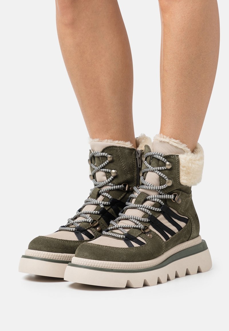 Bottes de randonnée vert olive avec un col doublé de fourrure, un tissu texturé, une semelle blanche épaisse et des lacets noirs et gris pour une meilleure adhérence.