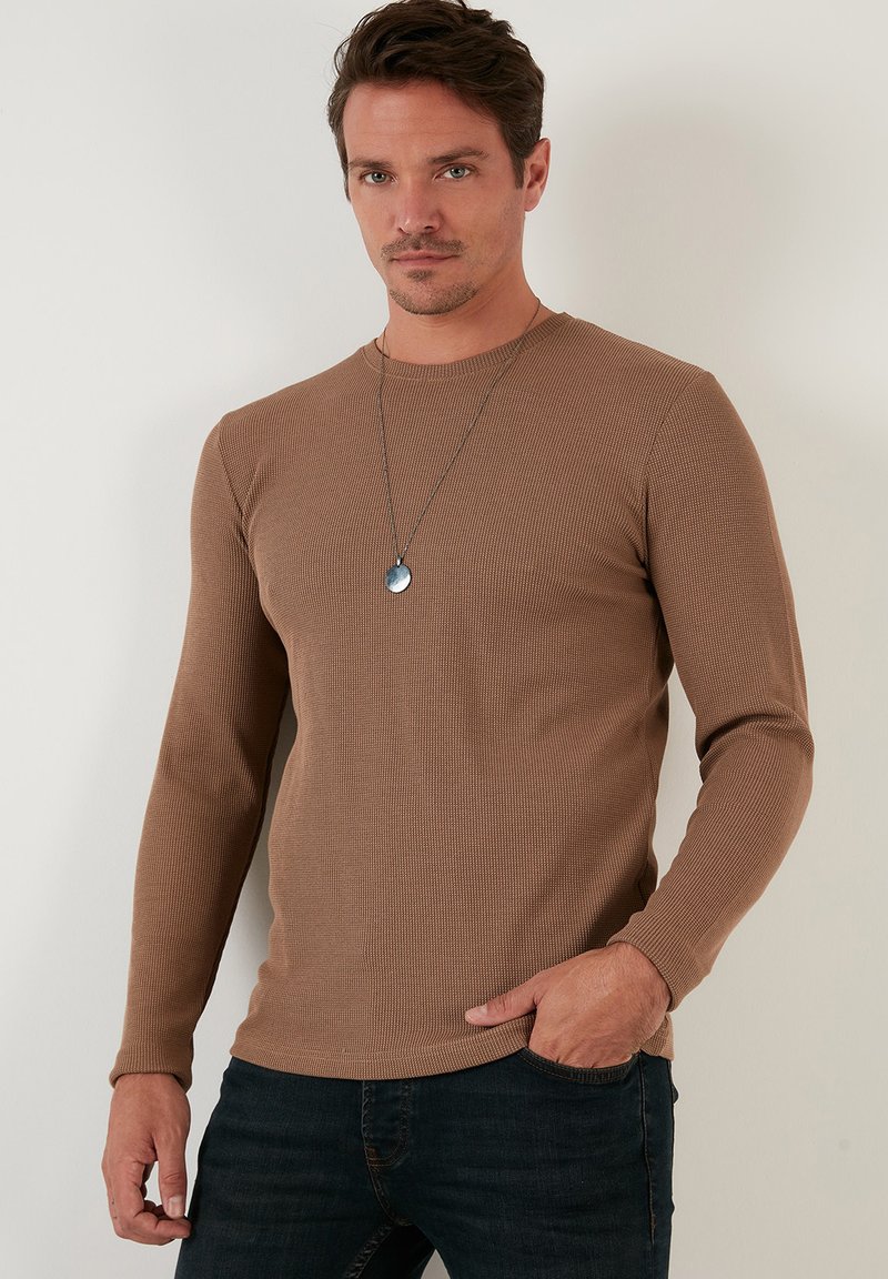 Braun gerippte Langarmshirt aus strukturiertem Stoff, mit rundem Ausschnitt und eng anliegendem Schnitt, kombiniert mit dunklen Jeans.